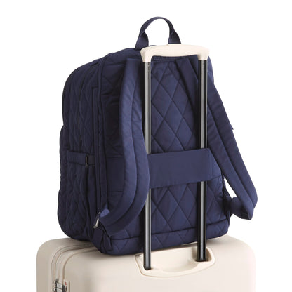 Navy quilted backpack on a beige suitcase with a white background